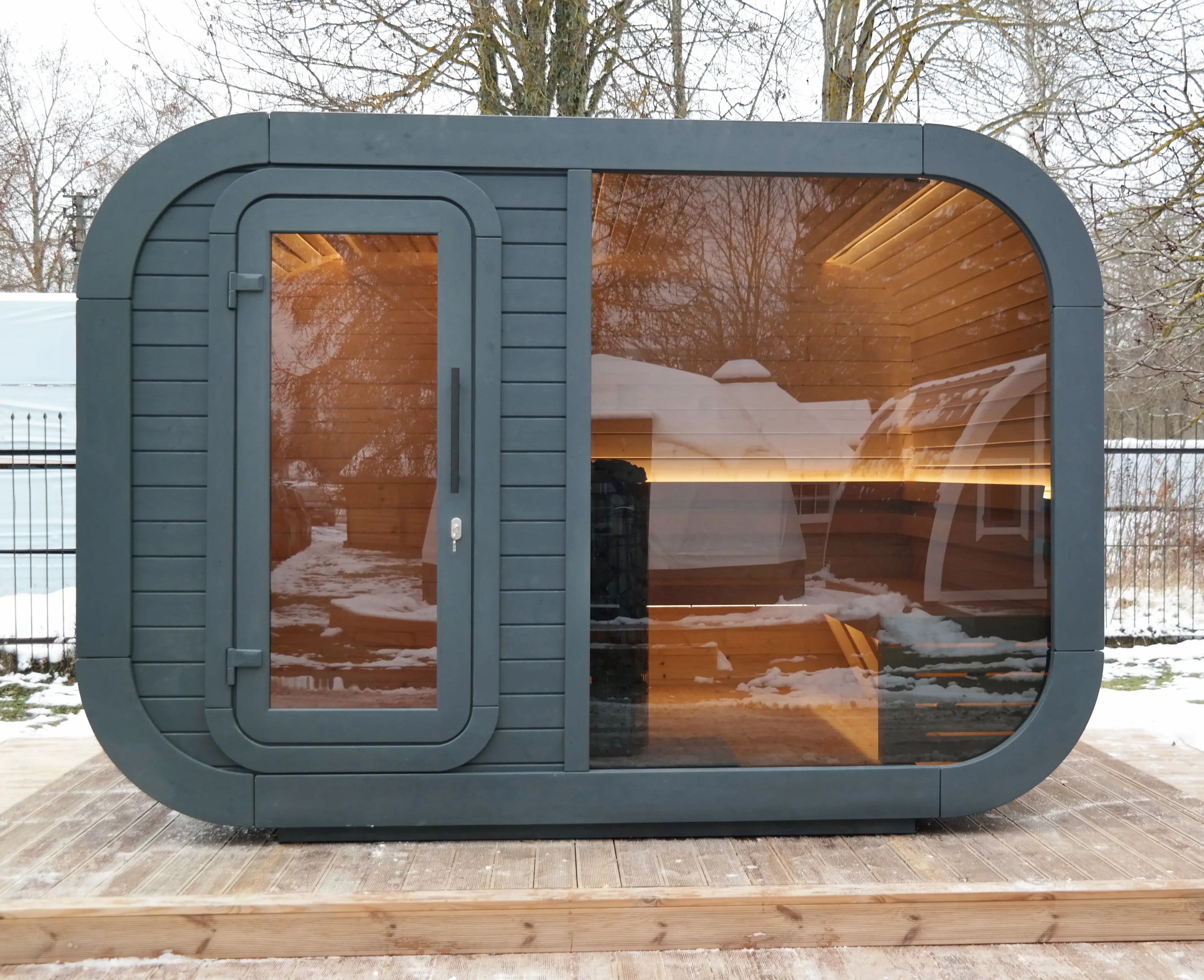 Front view of the Aurora luxury outdoor sauna pod with full glass window and changing room, set on a wooden deck in winter.