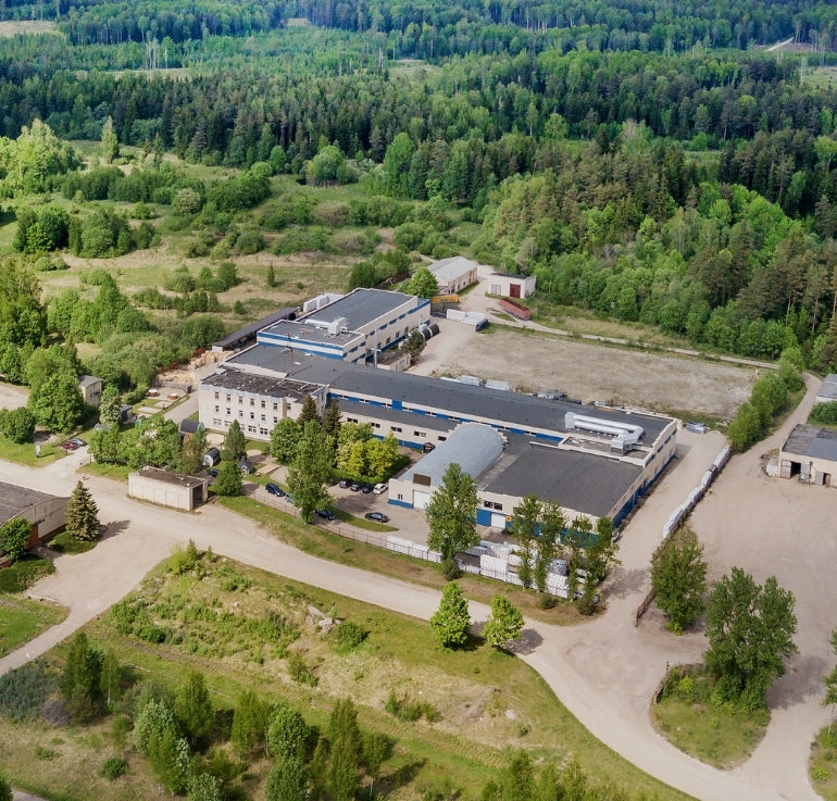 Aerial view of the GlampLaunch production facility surrounded by forest, showing the full-scale factory, yard space, and pods arranged for inspection.
