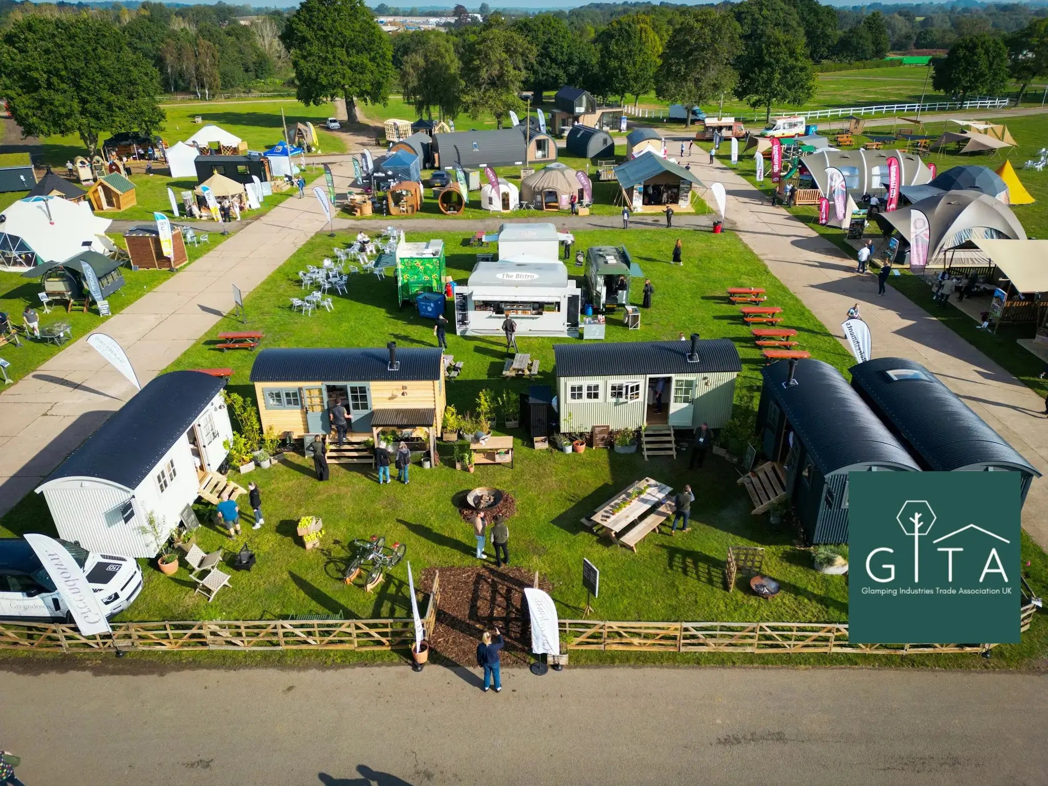 Aerial view of The Glamping Show at Stoneleigh Park, Warwickshire, with glamping pods, shepherd huts, and exhibitor stands on display at the industry’s leading trade event with a GITA (Glamping Industries Trade Association) logo in the bottom right corner.
