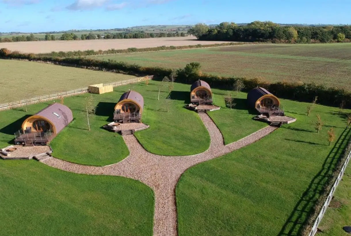 Aerial drone view of four modern glamping pods arranged in landscaped grounds in the UK countryside