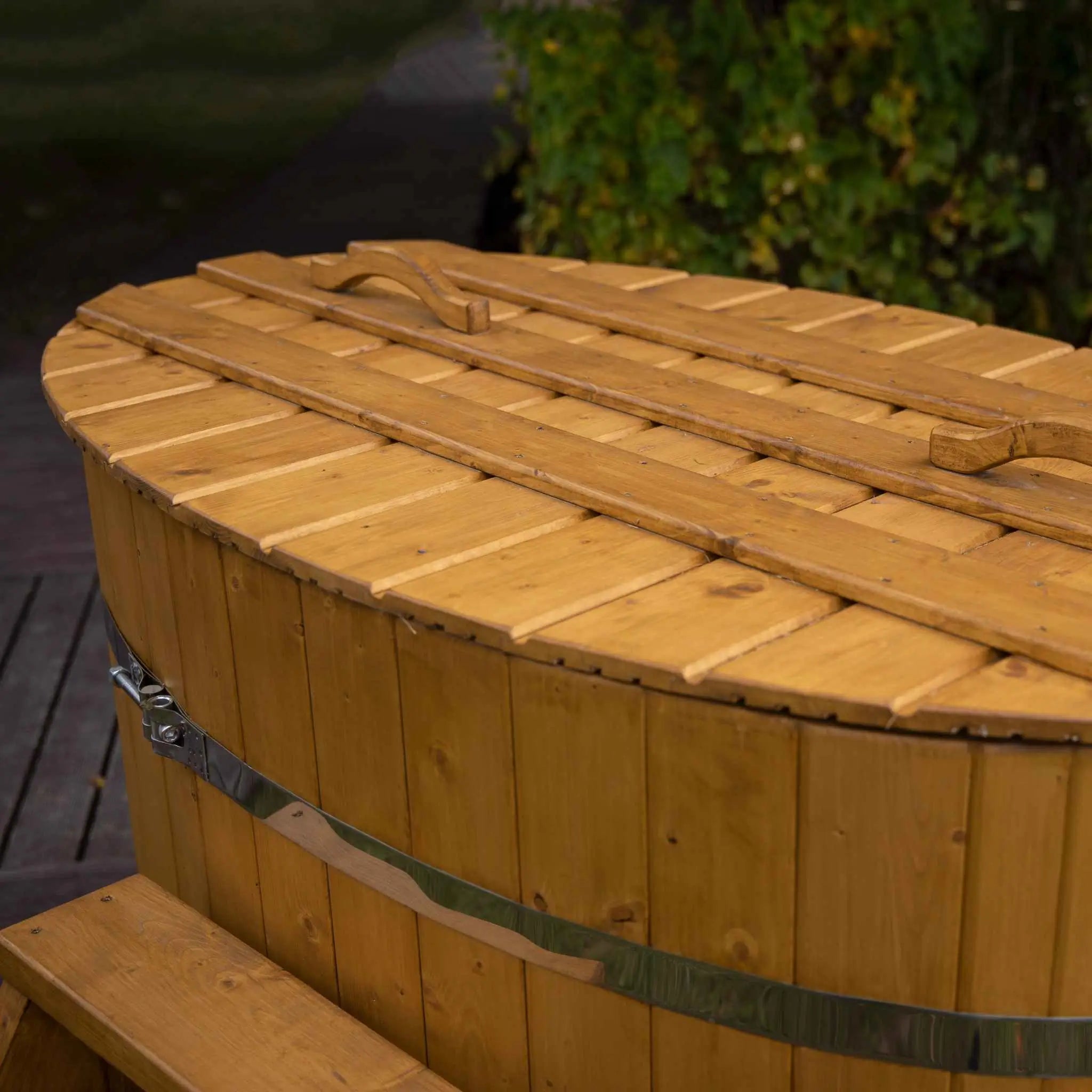 Oval-shaped wooden cold plunge tub with fitted lid and metal bands, designed for 1-2 people, placed outdoors.