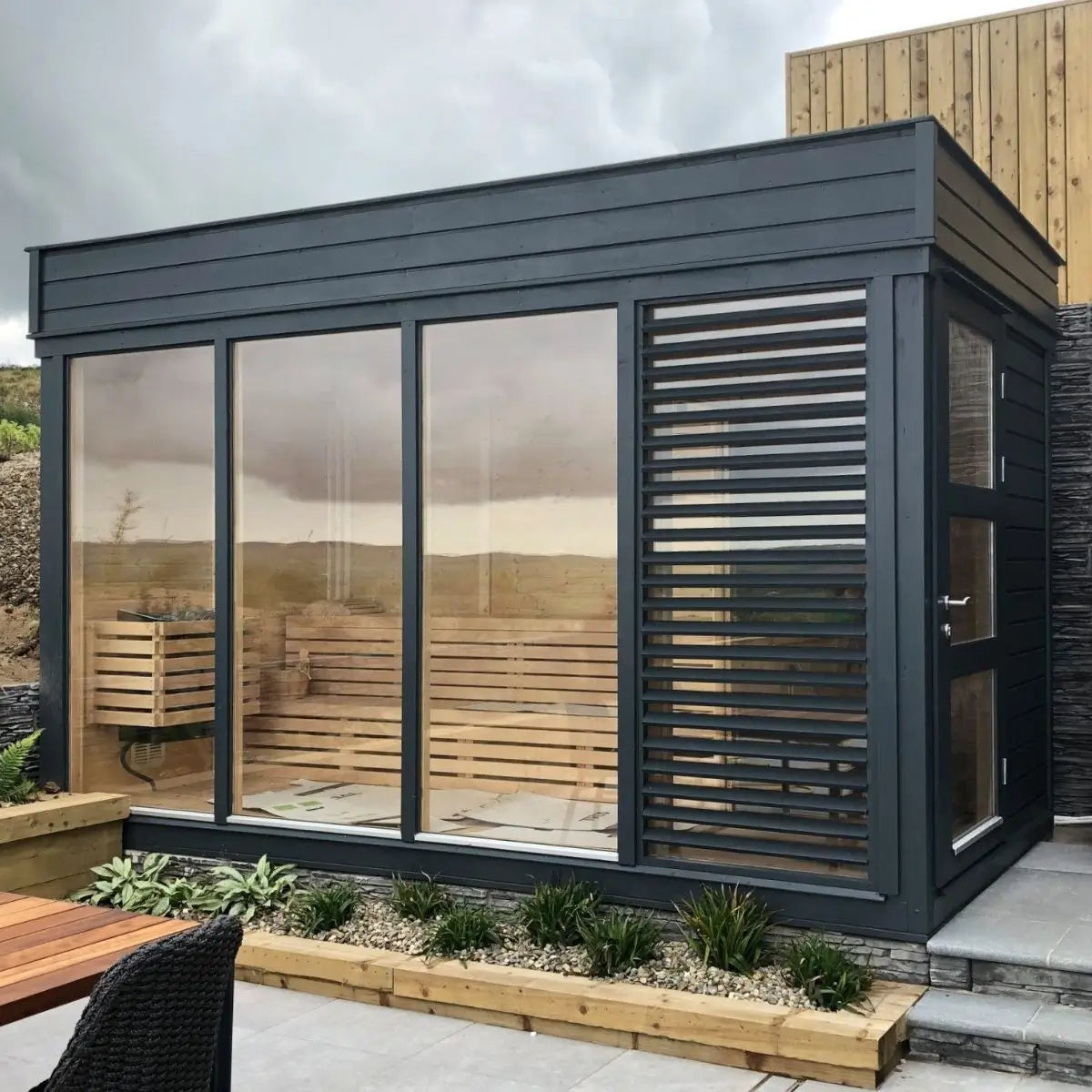 Modern outdoor cube sauna with large glass panels and a private changing room, ideal for 4–6 people seeking relaxation and stress relief in a garden or rural UK setting.