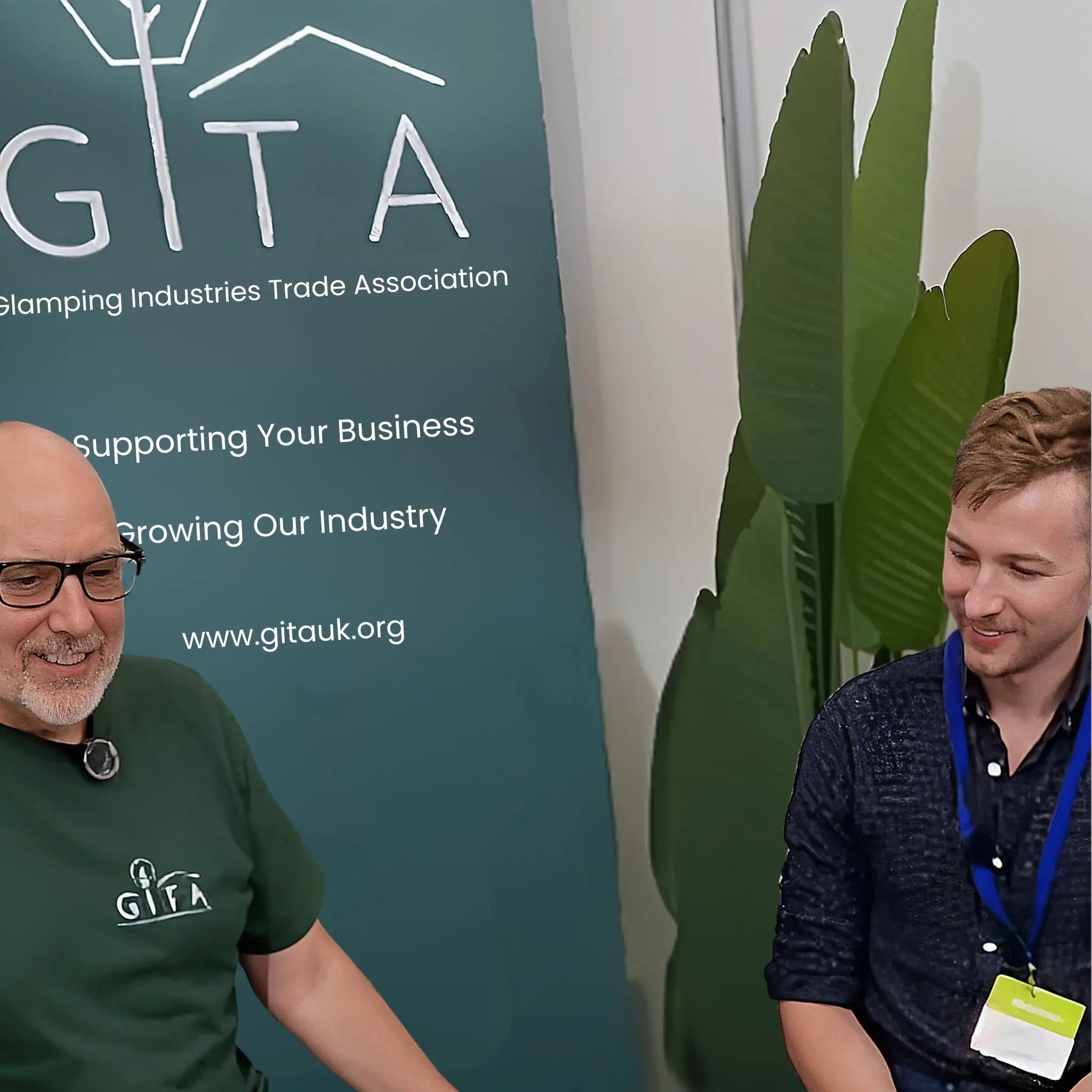 GITA Directors John and Taylor speaking together at the GITA stand during The Glamping Show 2025, discussing industry growth and collaboration.