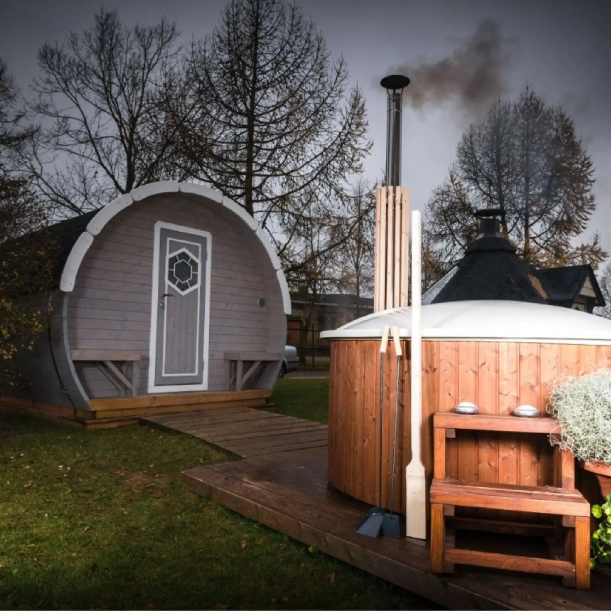Rustic outdoor setting with a steaming Finnish Ofuro-style wooden hot tub and a grey barrel glamping pod, ideal for relaxation and Scandinavian-style hydrotherapy.