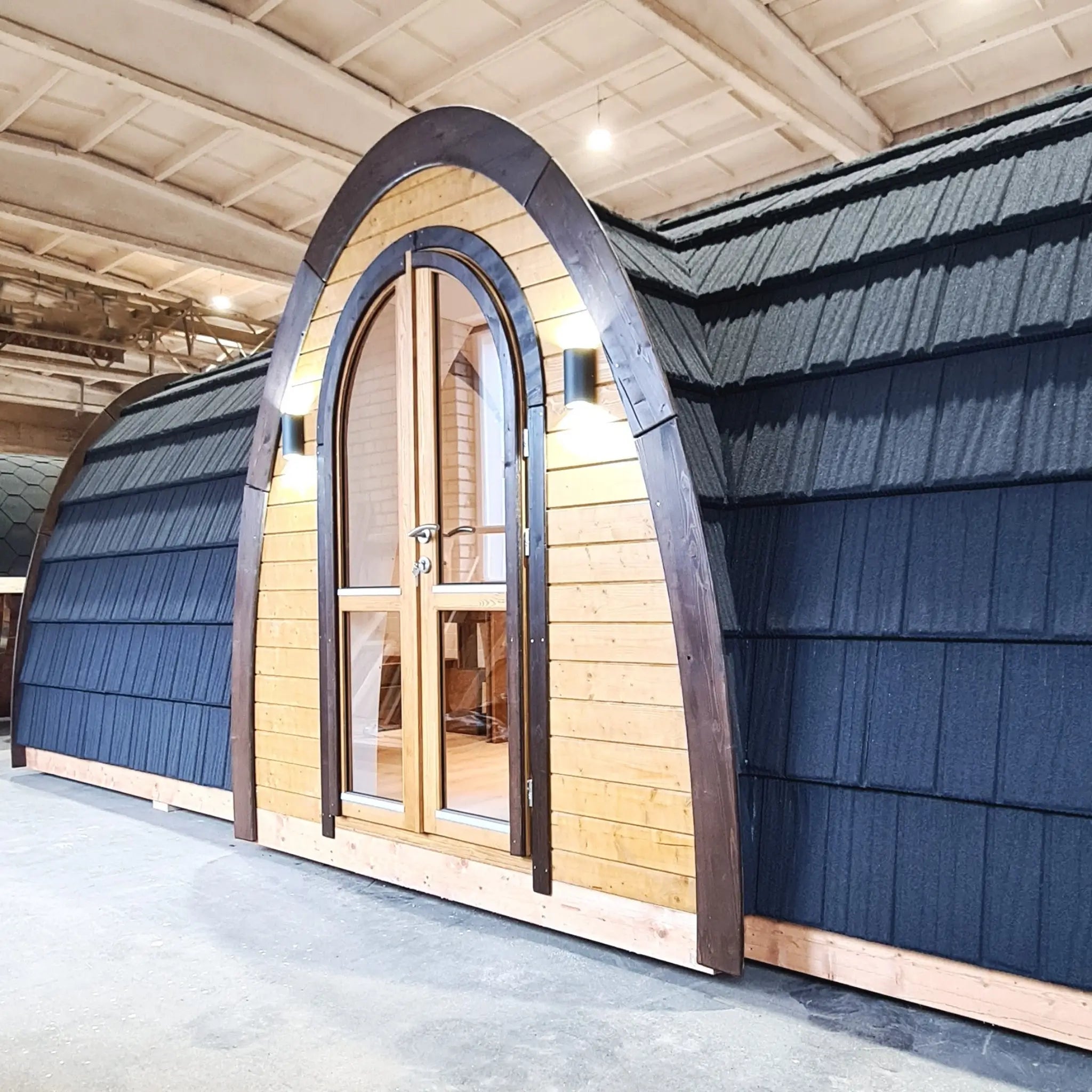 Modern arched glamping pod exterior with timber cladding and dark curved roof shown indoors during production