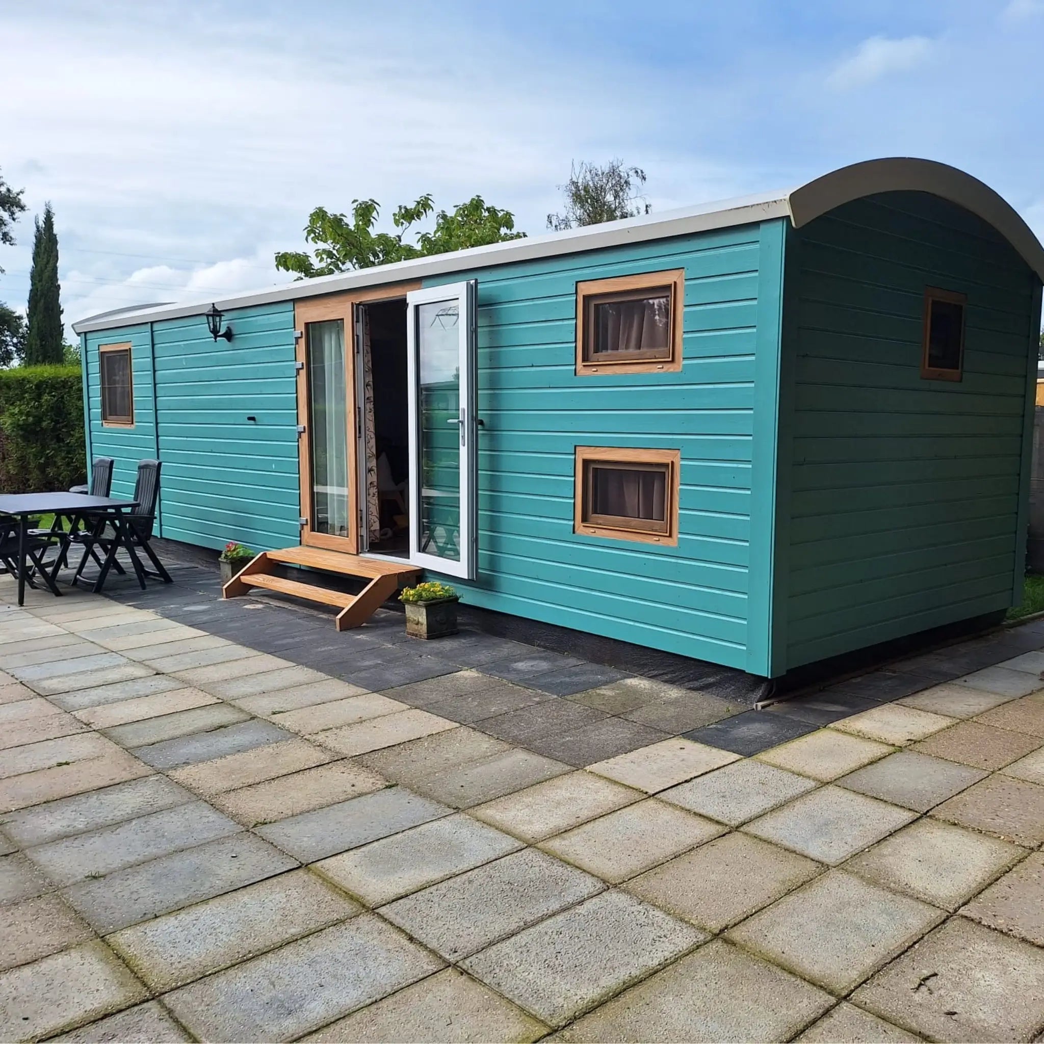 Contemporary shepherd’s hut with teal cladding and outdoor seating, offering sustainable off-grid accommodation.