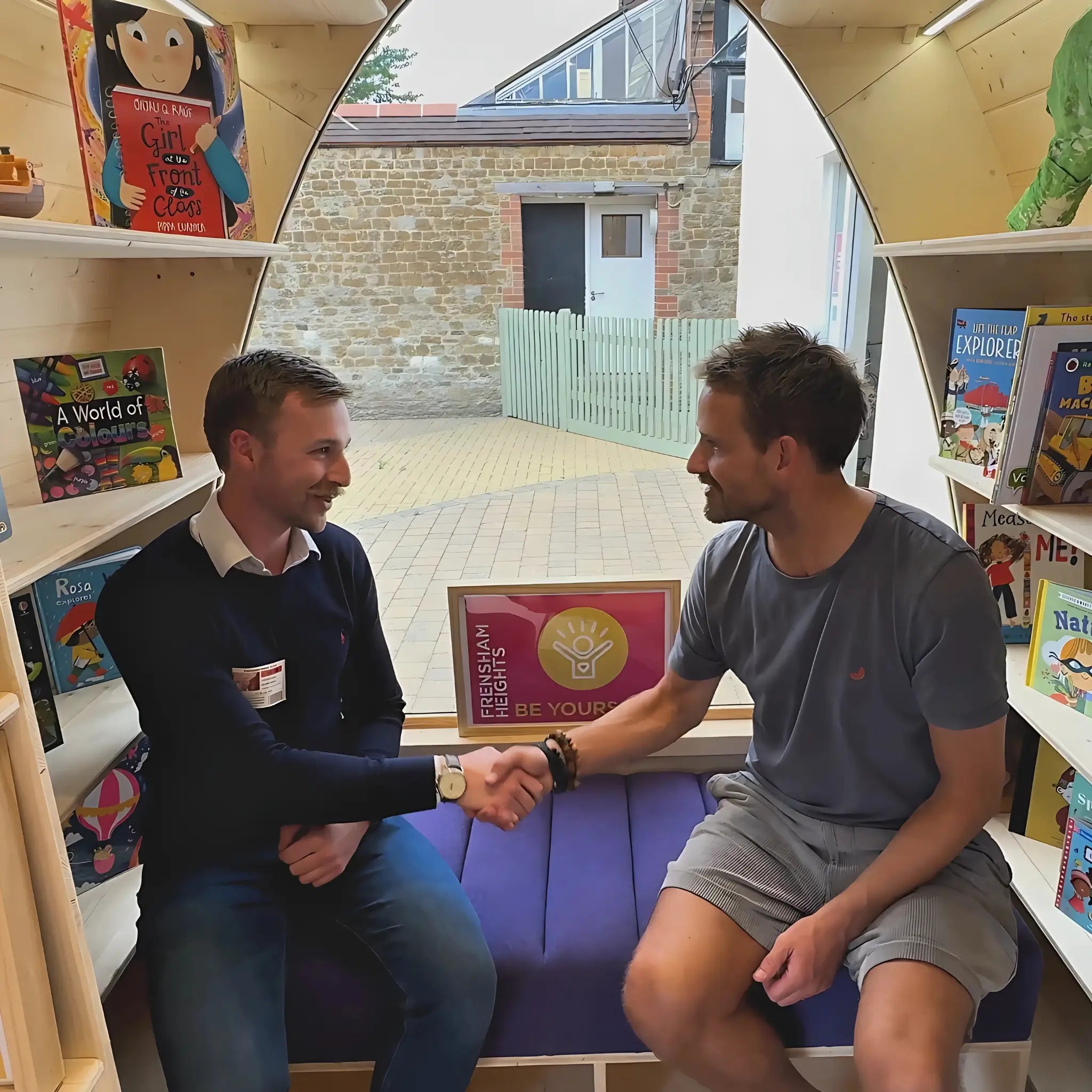 Taylor and the Head of the Junior School at Frensham Heights shaking hands inside a modular pod library surrounded by children’s books.