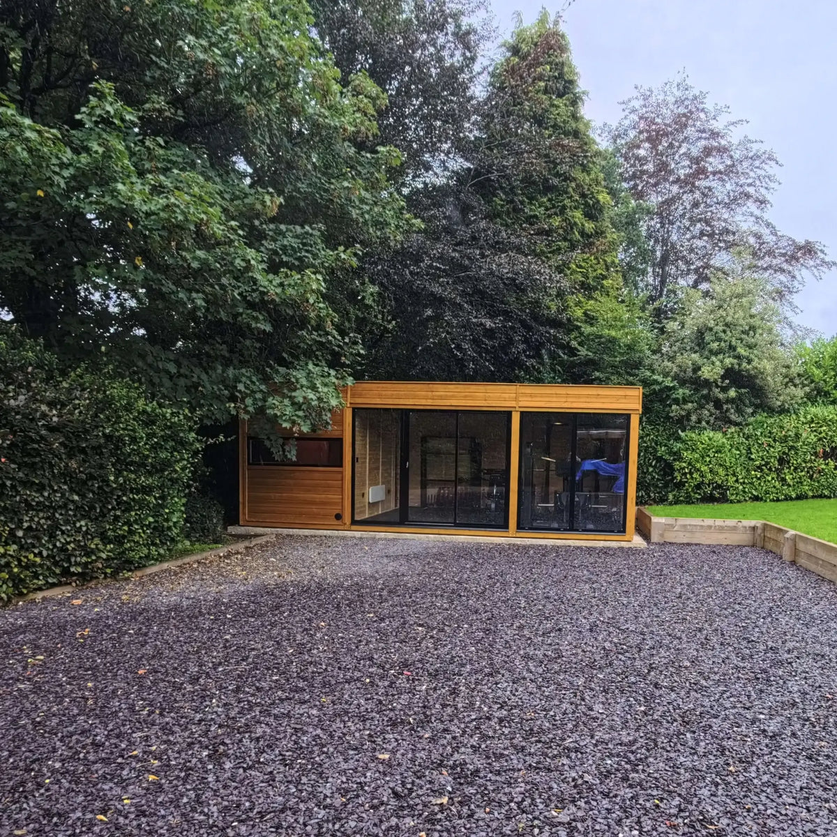 Wide front view of timber outdoor sauna and gym building with large glass doors in a garden setting