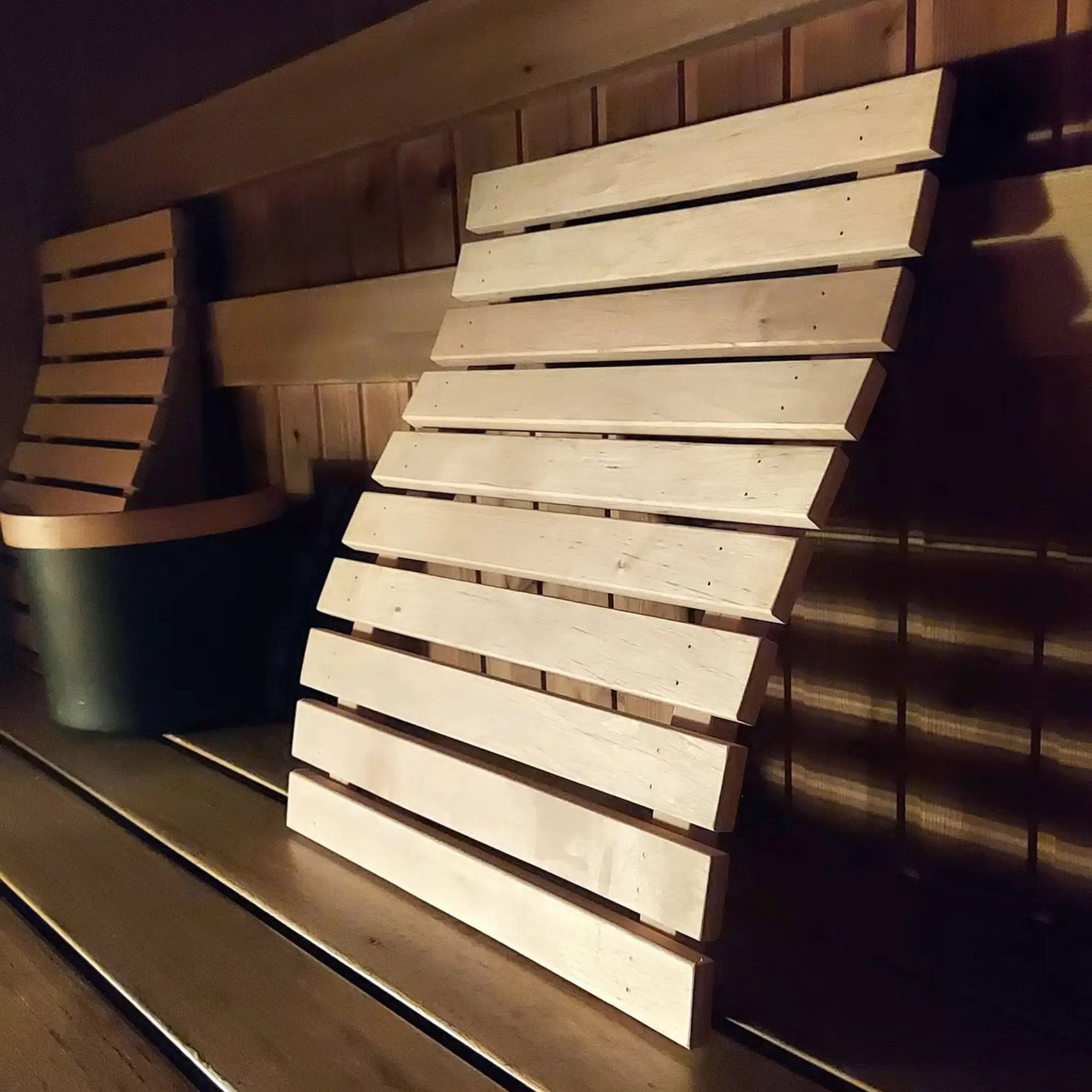 Wooden sauna bench backrest in use inside a sauna with warm lighting and timber bench seating