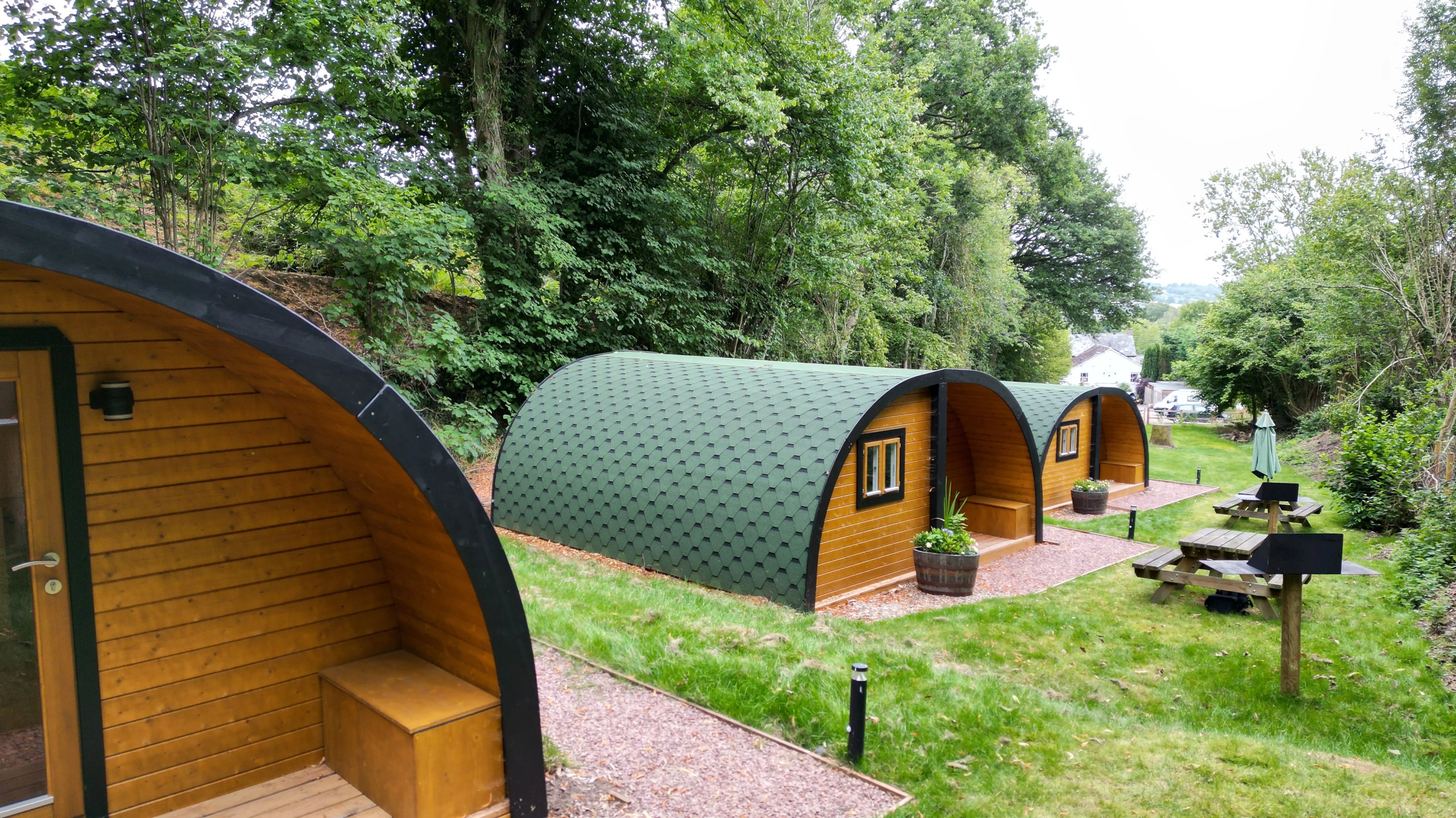 Bespoke wooden glamping pods at The Crown at Pantygelli in Abergavenny, surrounded by woodland with outdoor picnic and BBQ areas for guests.