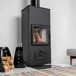 Black fireplace tool kit beside a modern black wood-burning stove with matching log carrier and stacked firewood.