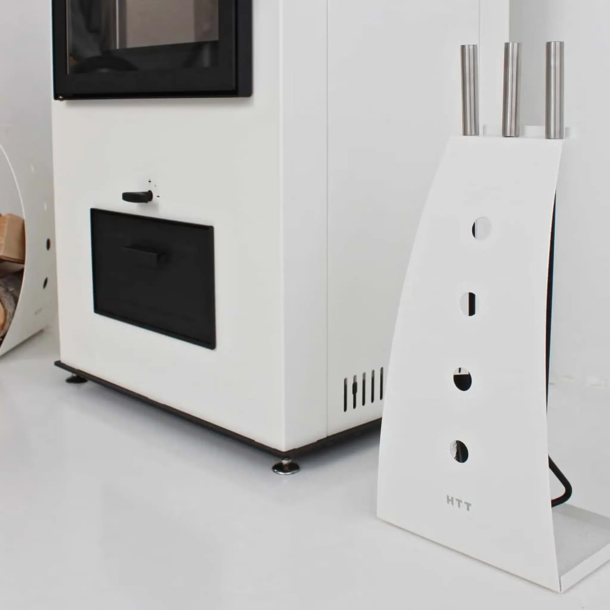 White fireplace tool kit beside a modern white fireplace, showing the curved steel stand and brushed nickel tool handles.