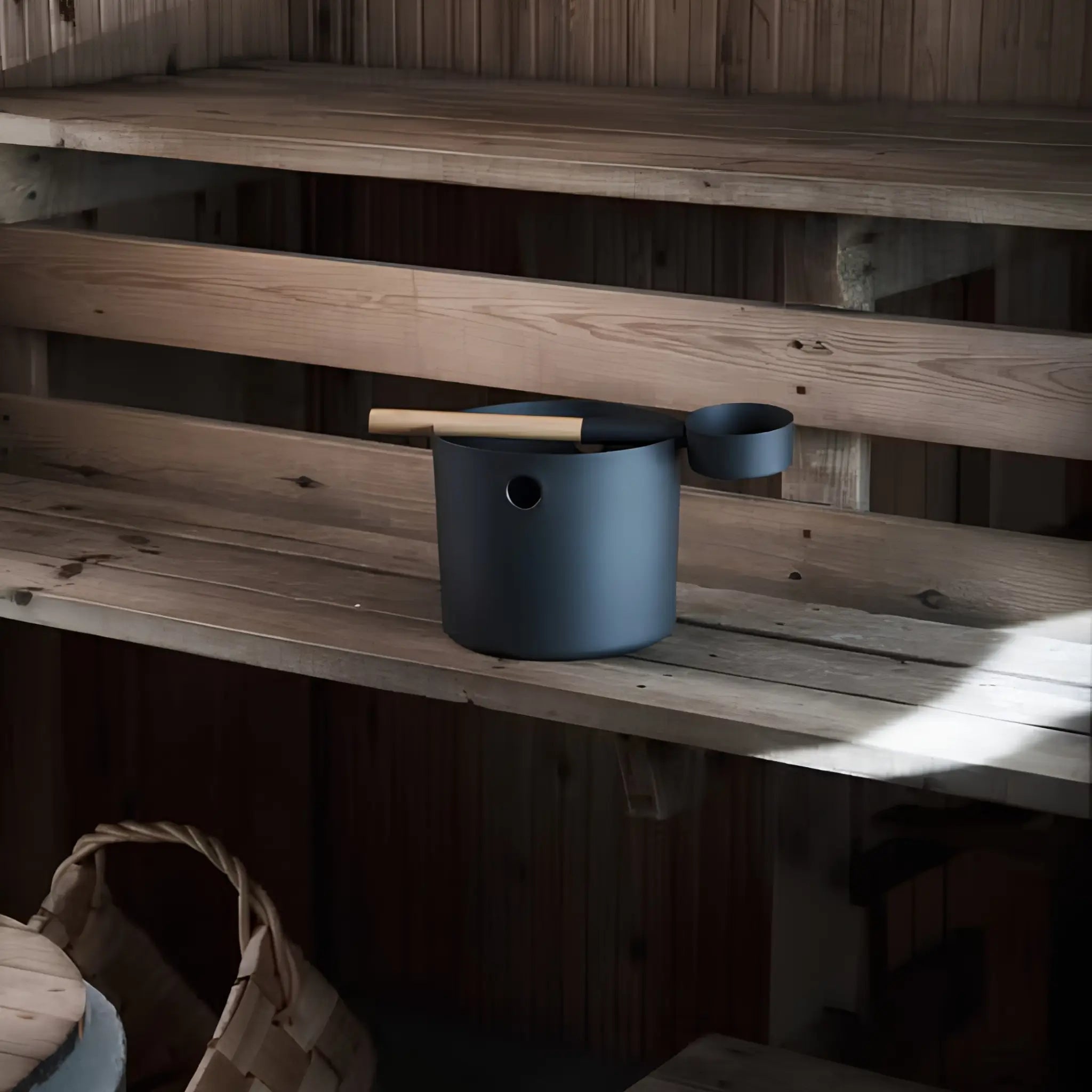 Black KOLO sauna pail and ladle placed on a wooden sauna bench inside a traditional sauna room.