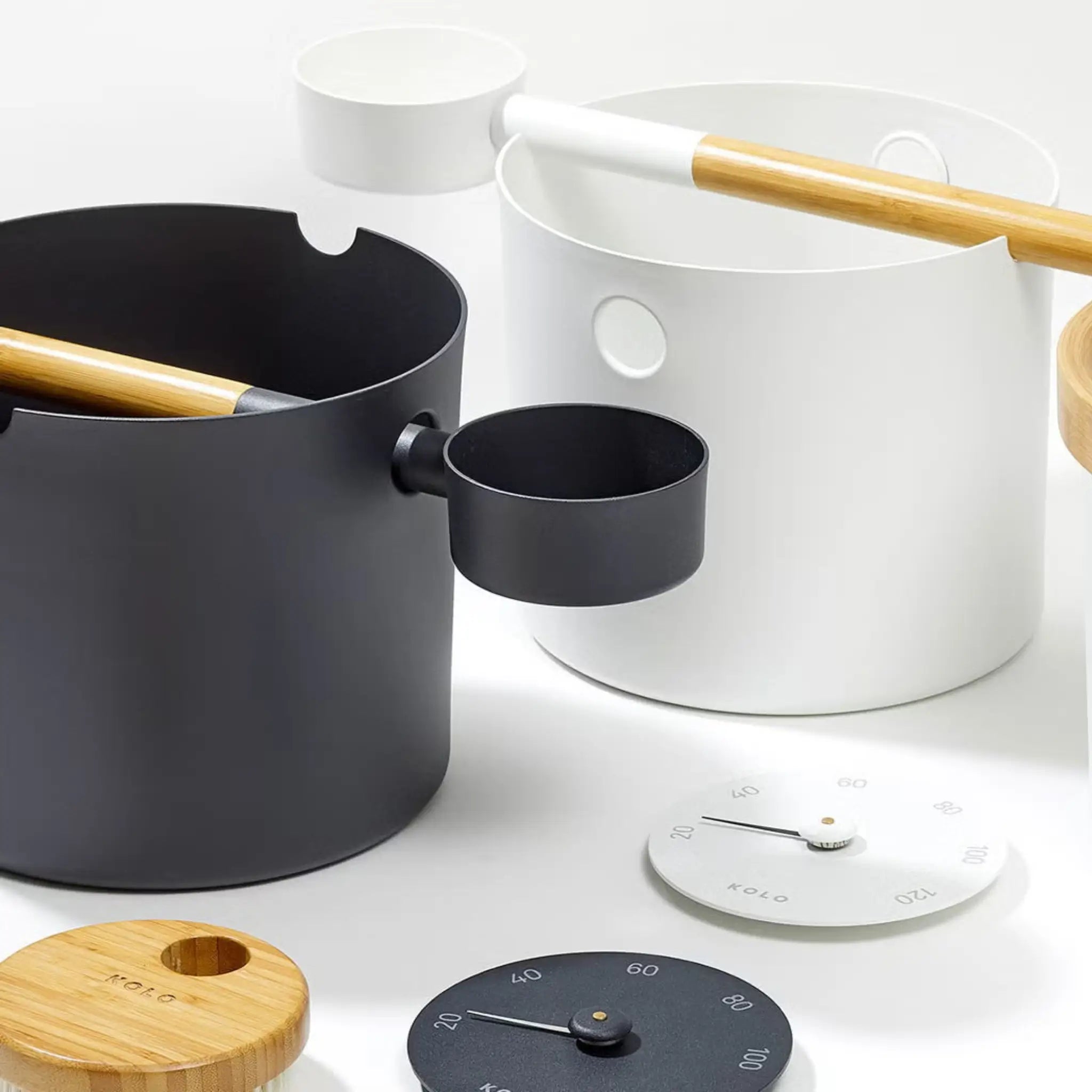 Black and white KOLO sauna pail and ladle sets displayed with matching sauna accessories.