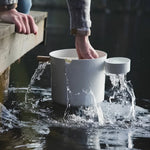 White KOLO sauna pail and ladle being used for water by a lakeside sauna setting.