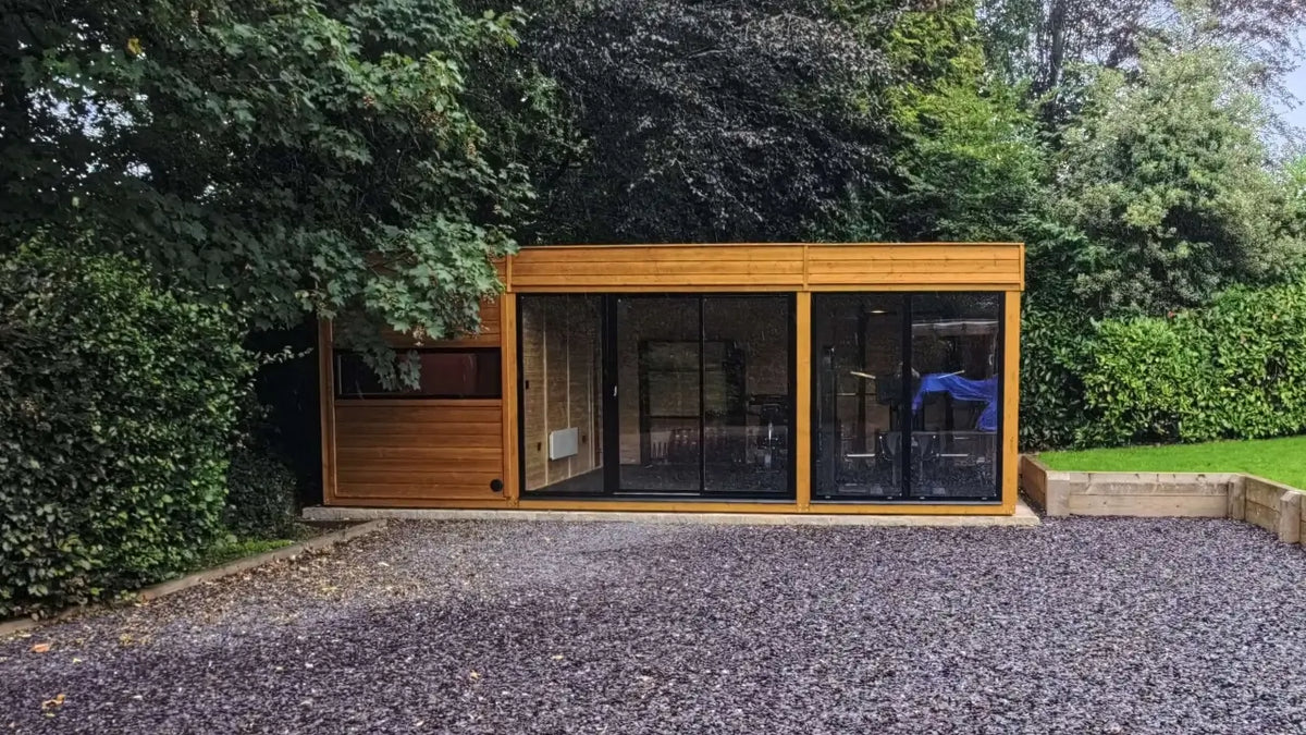 Wide front view of timber outdoor sauna and gym building with large glass doors in a garden setting