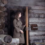 Woman wearing a brown Rento Kenno bathrobe outside a rustic wooden sauna cabin.