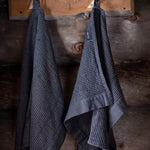 Black Rento Kenno hand towels hanging on a rustic wooden sauna wall.