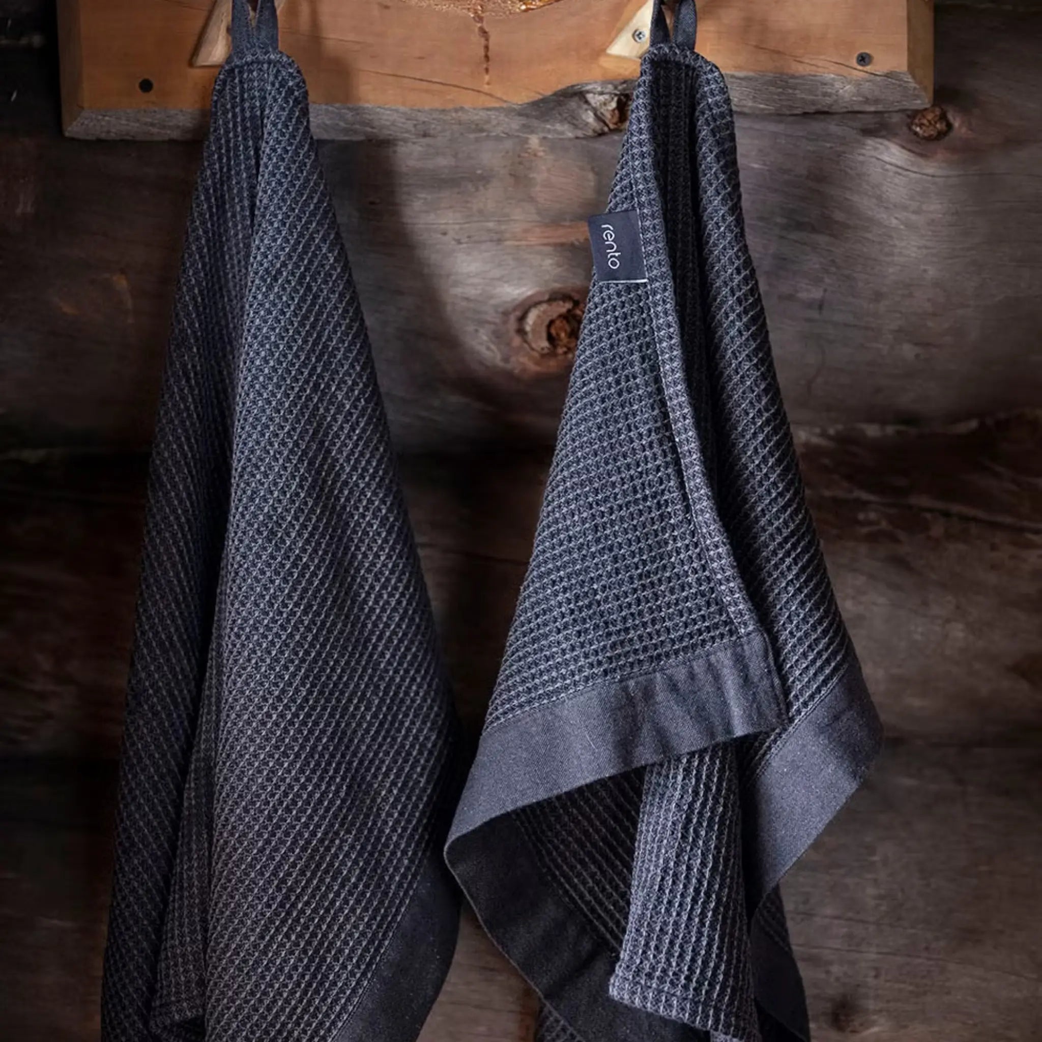 Black Rento Kenno hand towels hanging on a rustic wooden sauna wall.