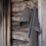 Brown Rento Kenno hand towel hanging on a wooden sauna wall with a matching sauna hat.