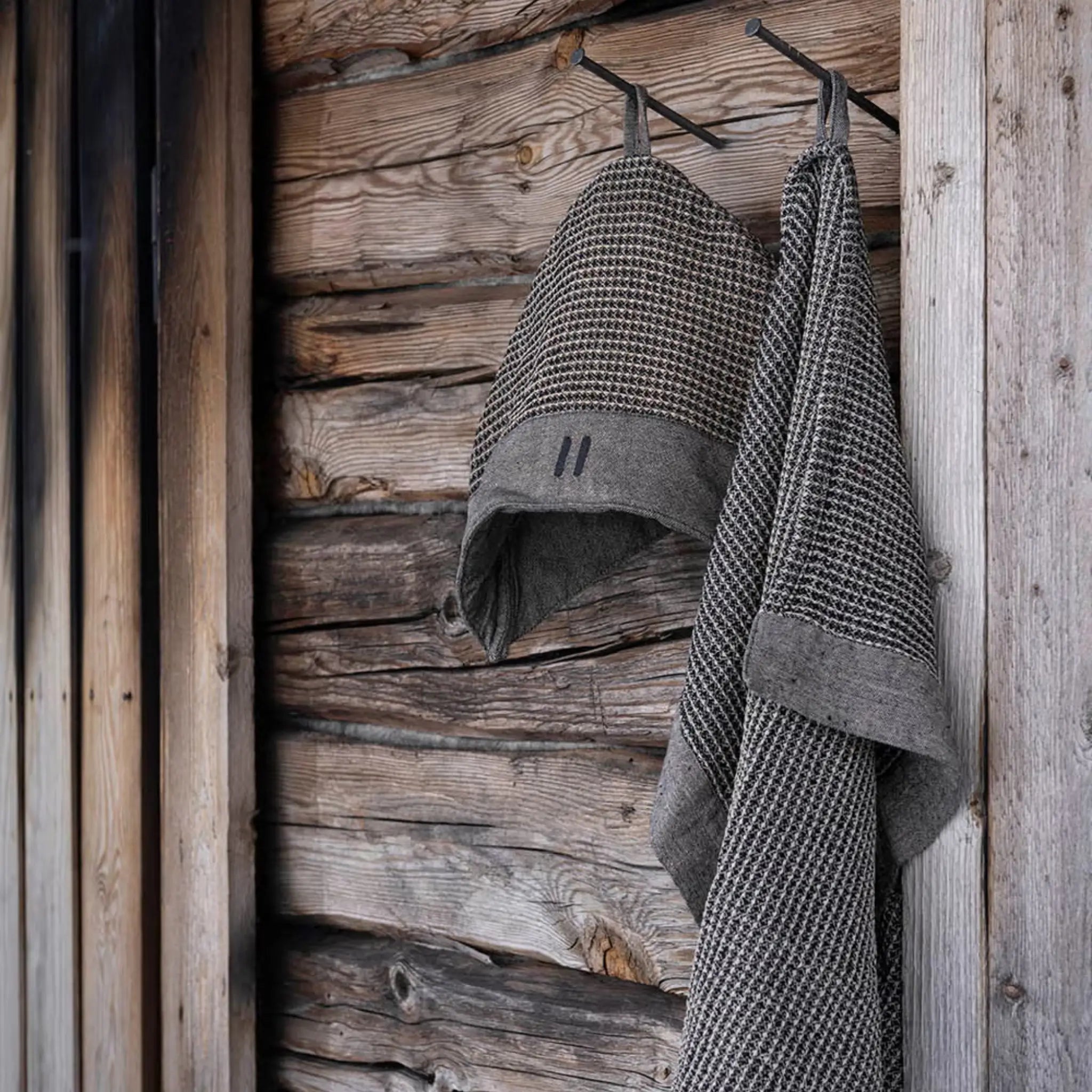 Brown Rento Kenno hand towel hanging on a wooden sauna wall with a matching sauna hat.