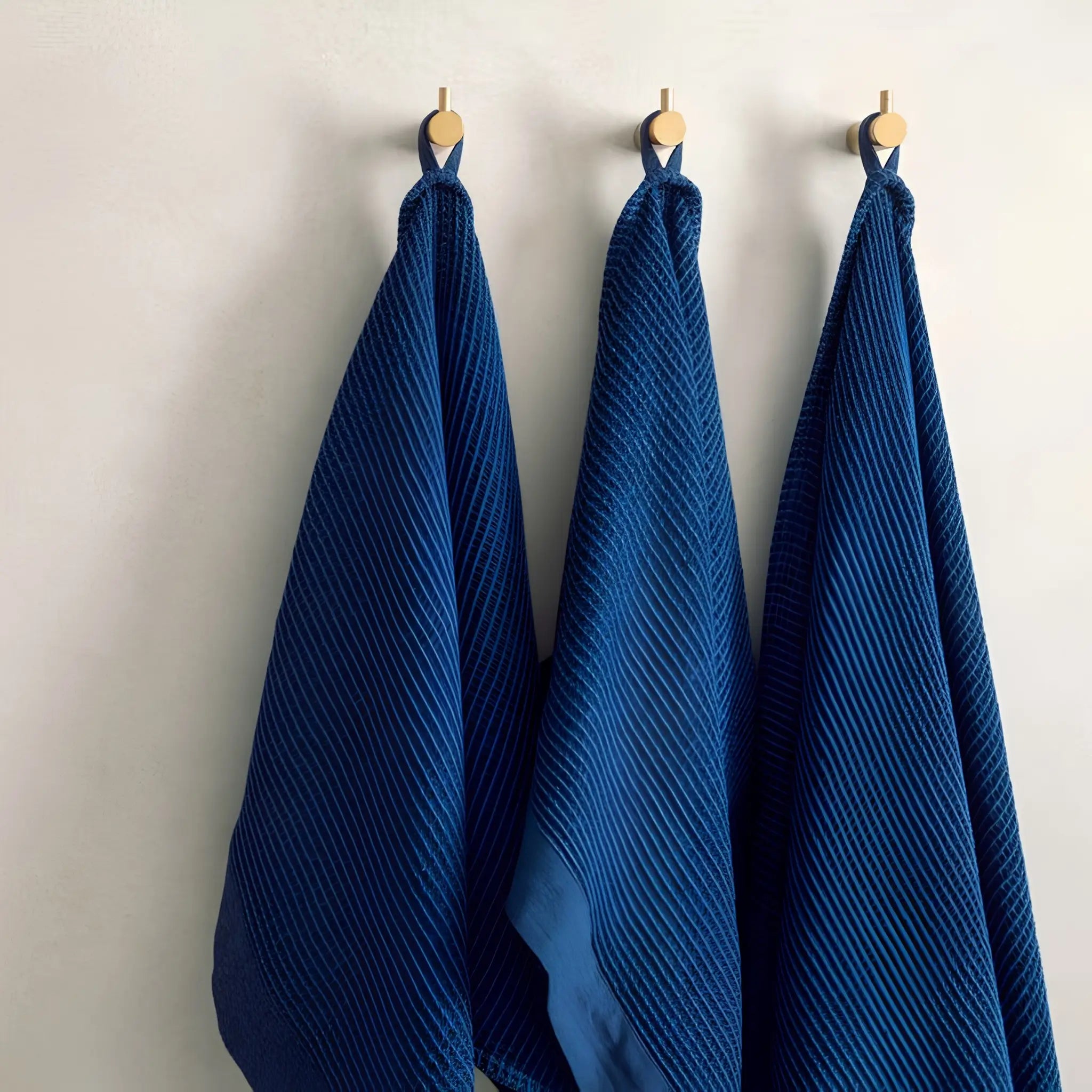Dark blue Rento Kenno hand towels hanging on a rustic log wall.