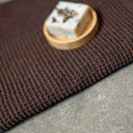 Dark brown Rento Kenno hand towel with textured weave and sauna soap on a wooden dish.