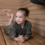 Child relaxing on a sauna bench in a brown Rento Kenno kids bathrobe