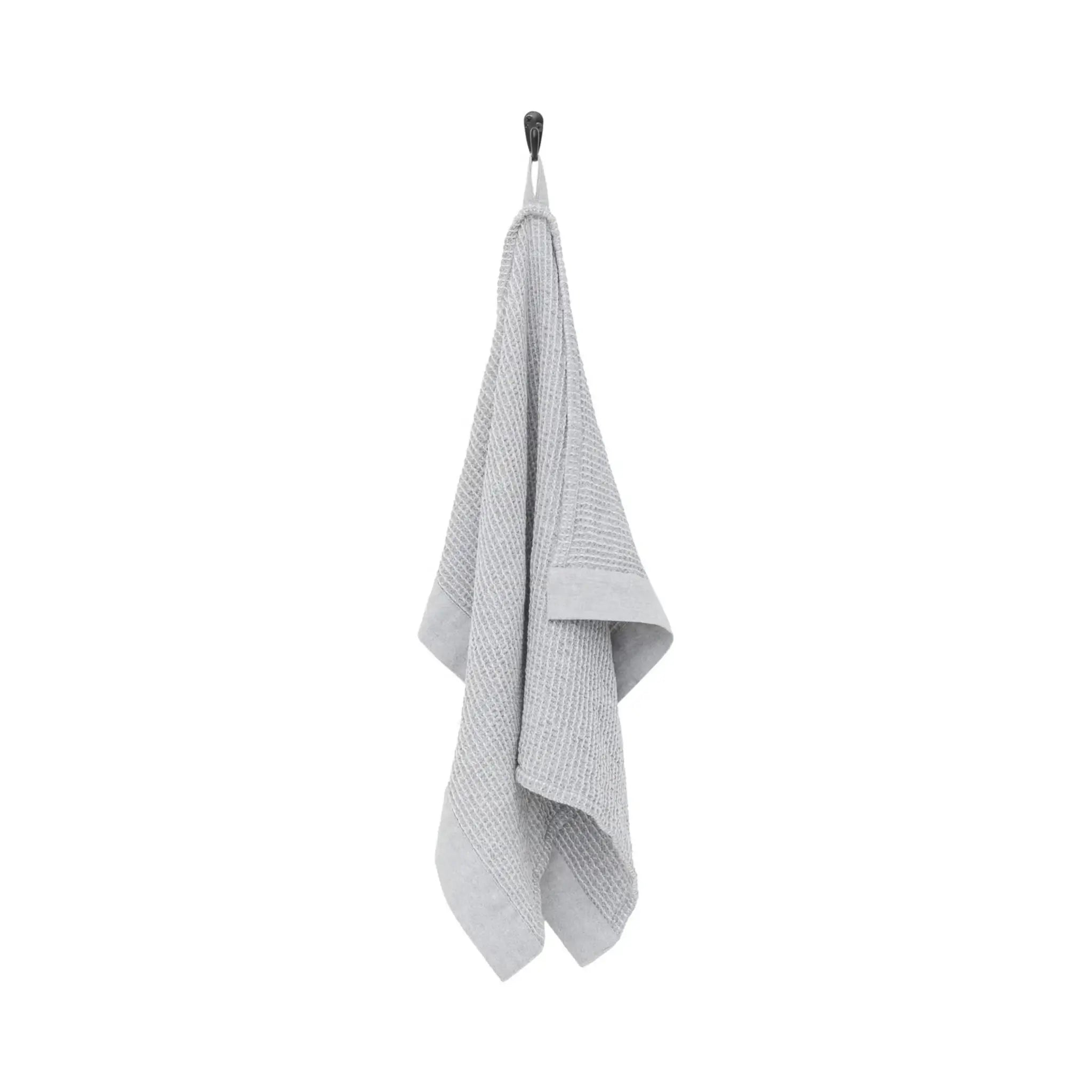 Grey and white Rento Kenno hand towels stacked on a wooden bench in a sauna setting.