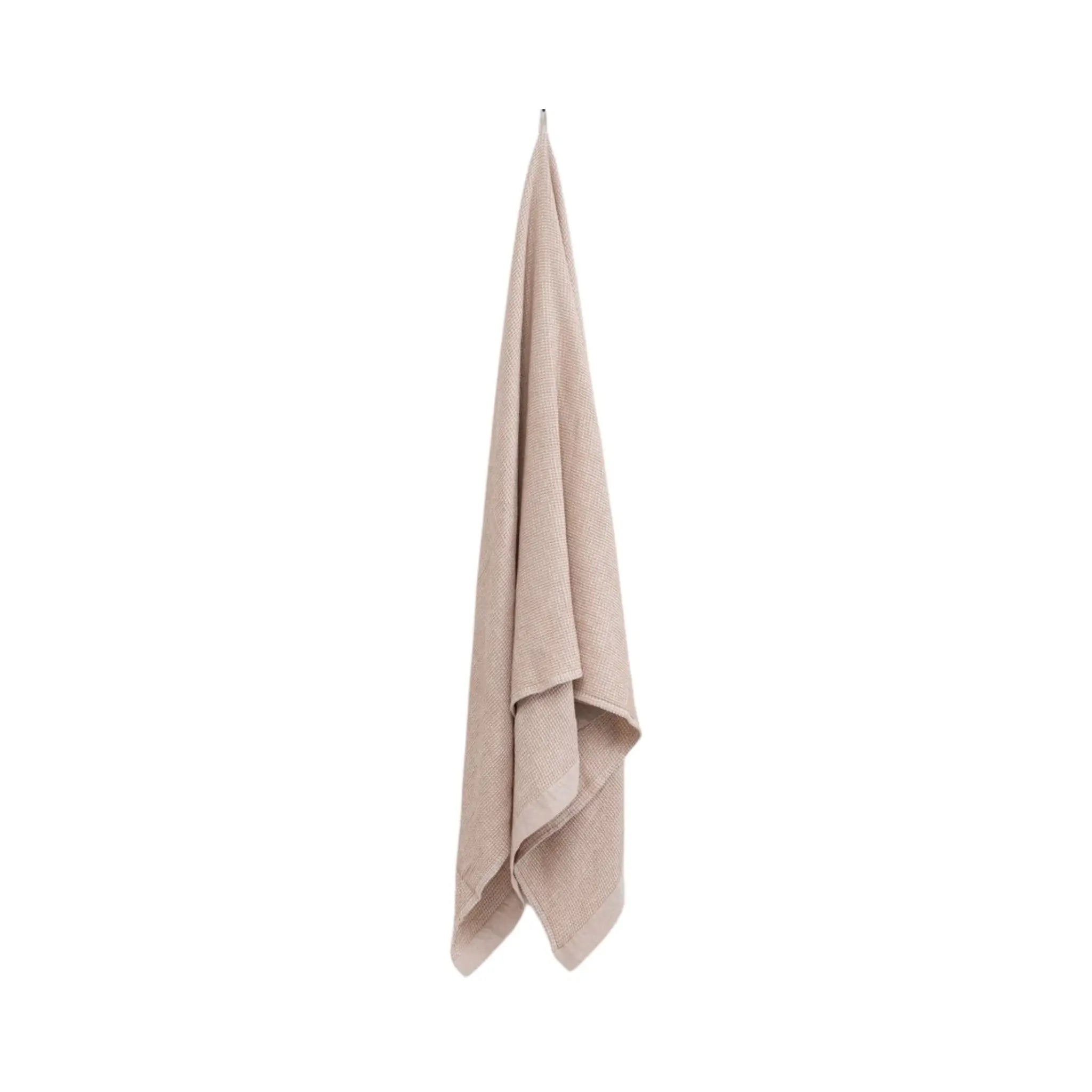 Beige large bath towel hanging on a white background showing soft waffle texture and chambray edging