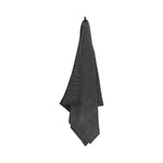 Black large bath towel hanging on a white background with textured weave and dark chambray border