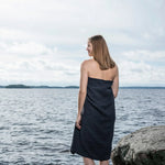 Black large bath towel worn as a sauna wrap by a woman standing beside a lake