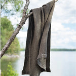 Brown waffle texture bath towel hanging from a tree branch beside a lakeside setting
