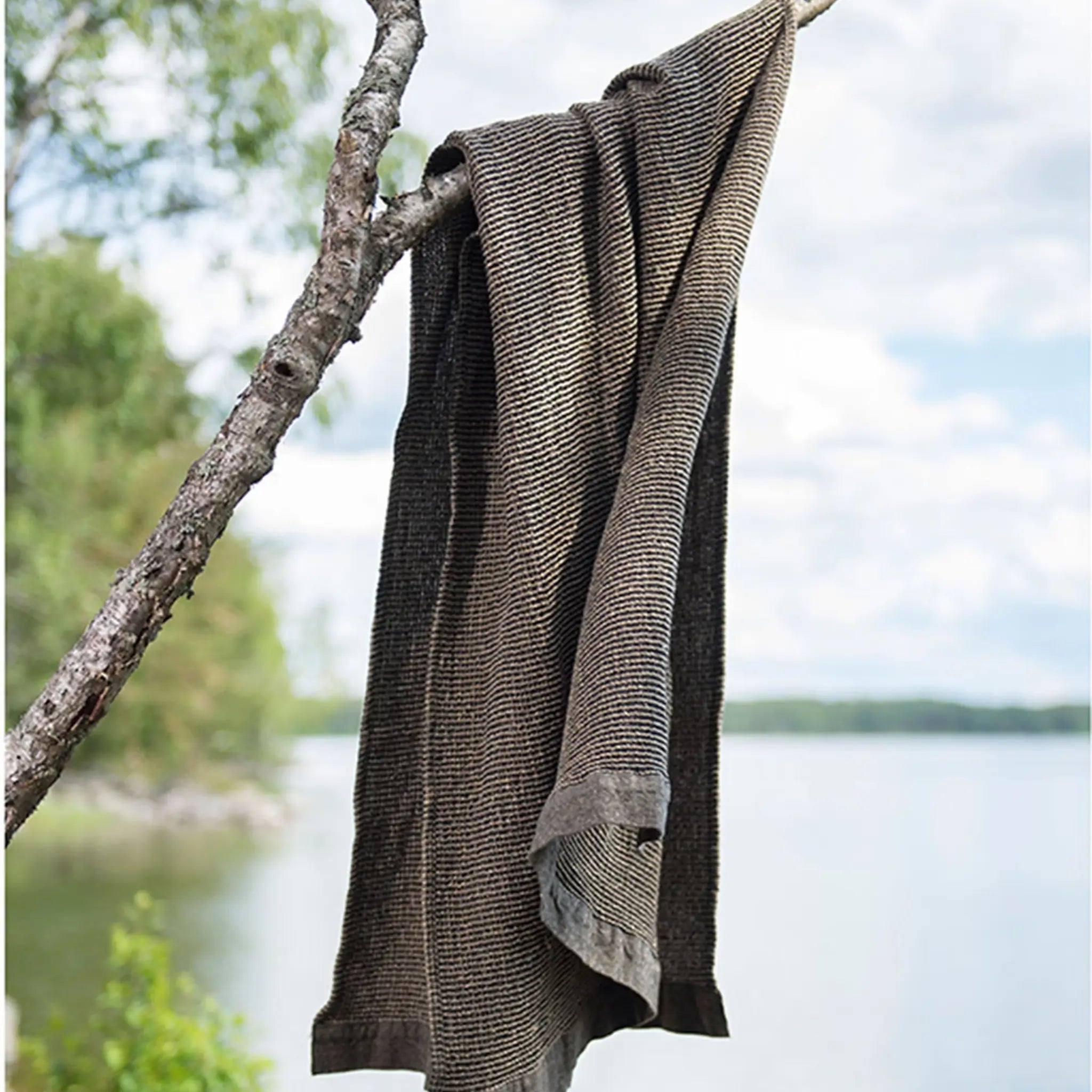 Brown waffle texture bath towel hanging from a tree branch beside a lakeside setting