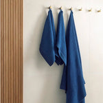 Dark blue waffle texture bath towels hanging on wall hooks in a modern sauna or bathroom setting