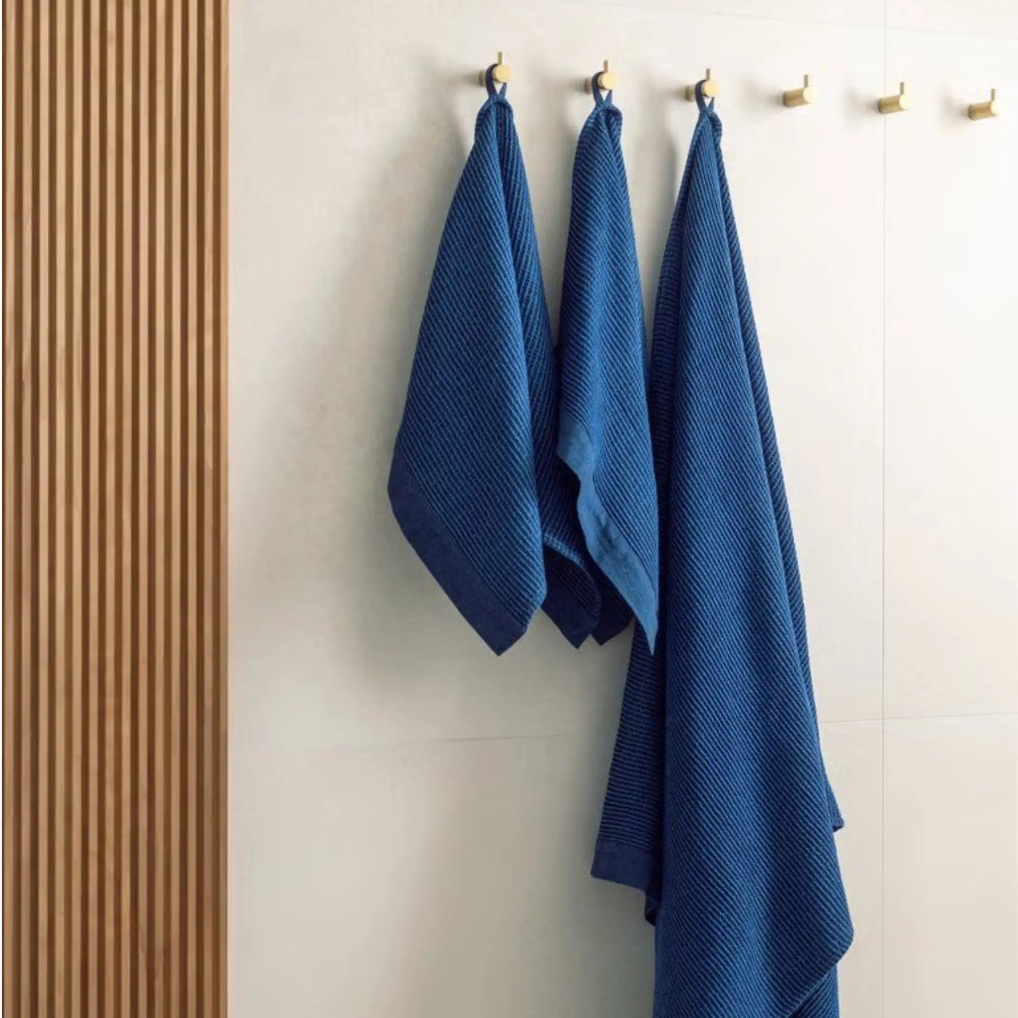 Dark blue waffle texture bath towels hanging on wall hooks in a modern sauna or bathroom setting