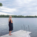 Woman wrapped in a dark green waffle texture bath towel standing on a wooden jetty by a lake