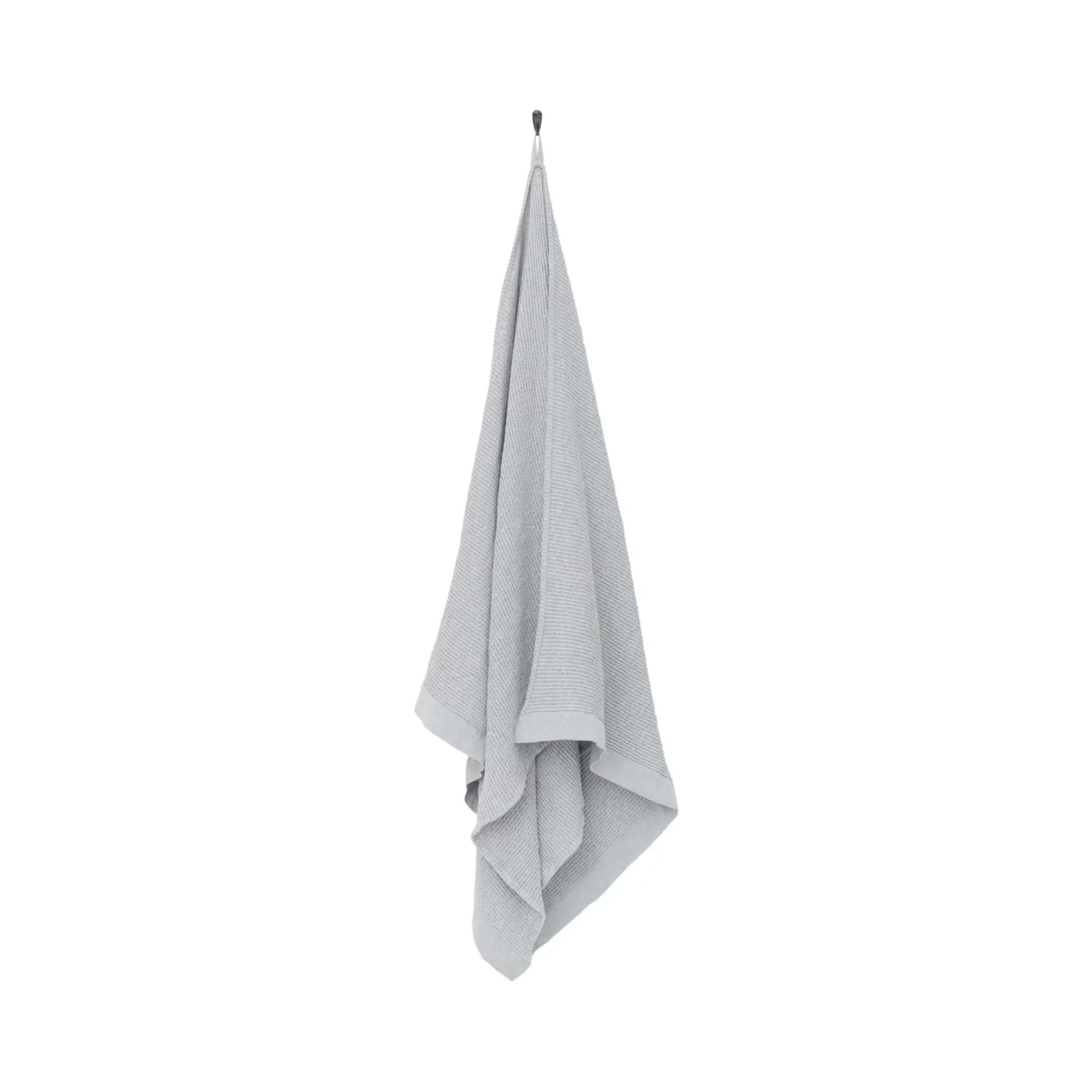 Grey white waffle texture bath towel hanging on a white background with soft recycled cotton blend fabric and chambray edging