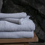Grey white waffle texture bath towels neatly stacked on a wooden stool in a spa setting