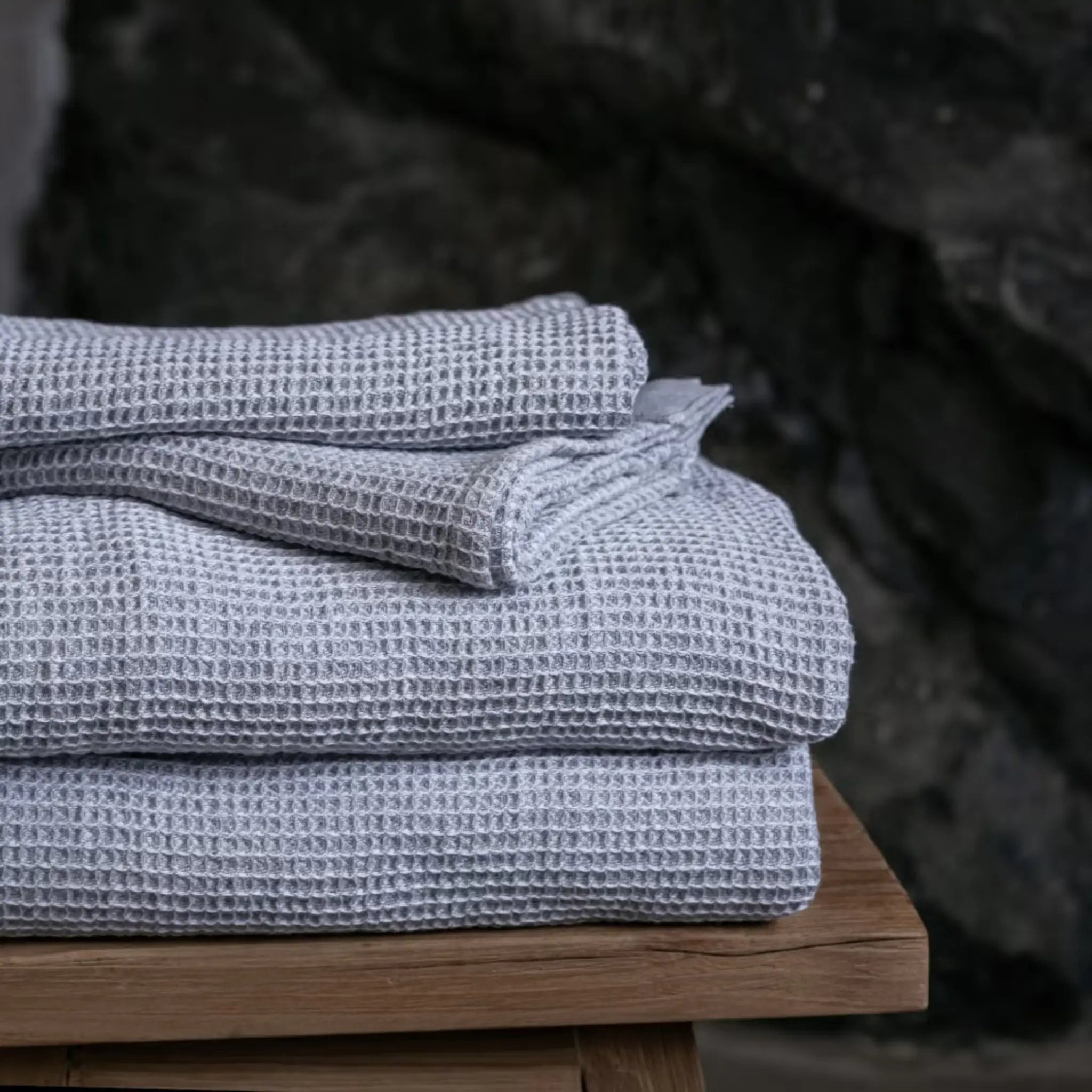 Grey white waffle texture bath towels neatly stacked on a wooden stool in a spa setting