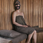 Brown Rento Kenno long sauna seat cover with matching pillow used by a woman relaxing in a sauna