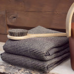 Brown Rento Kenno sauna seat cover folded on a sauna bench with body brush and sauna bucket