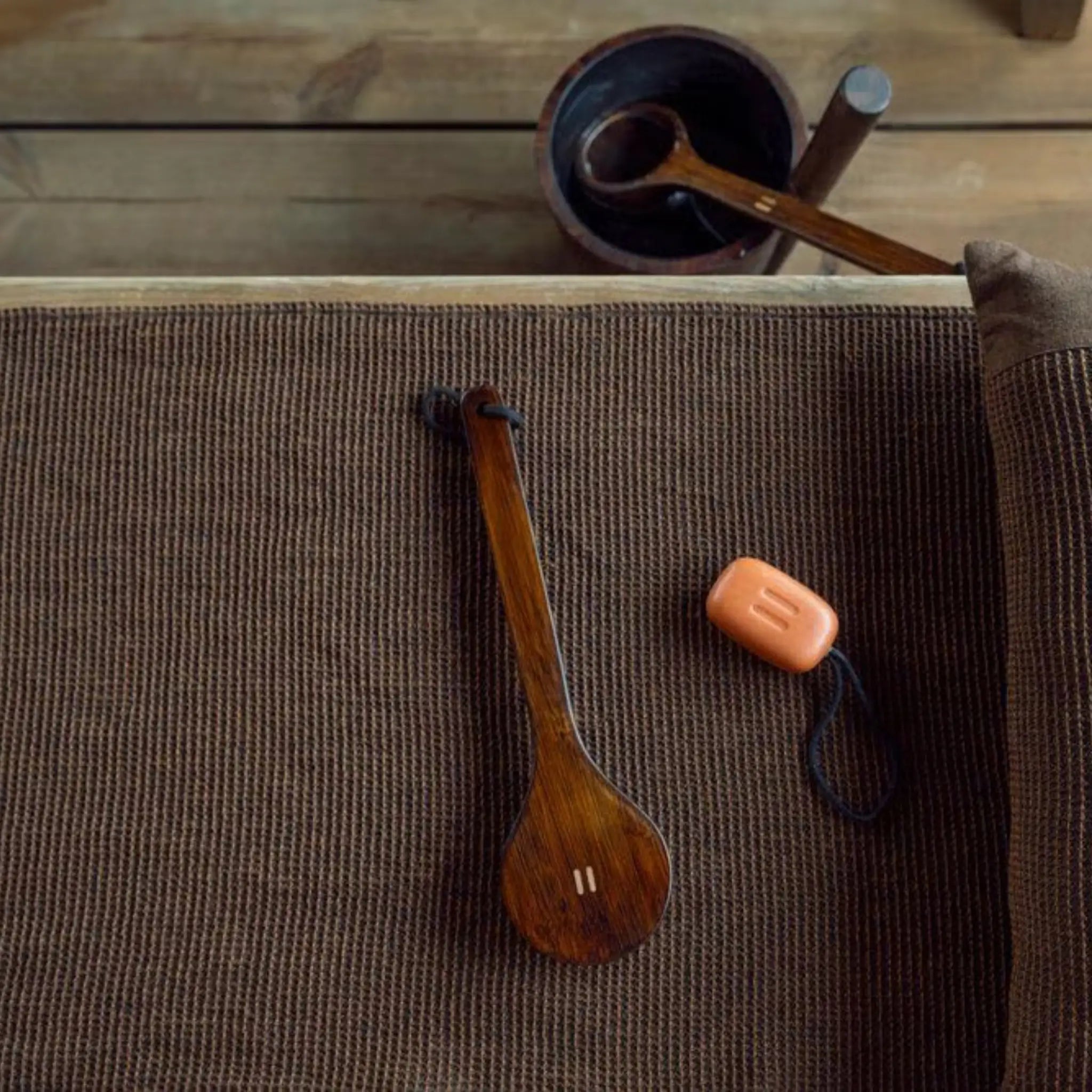 Dark brown Rento Kenno sauna seat cover on a bench with wooden ladle and bar soap