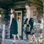 Couple walking outside a log sauna wearing dark green matching sauna wraps