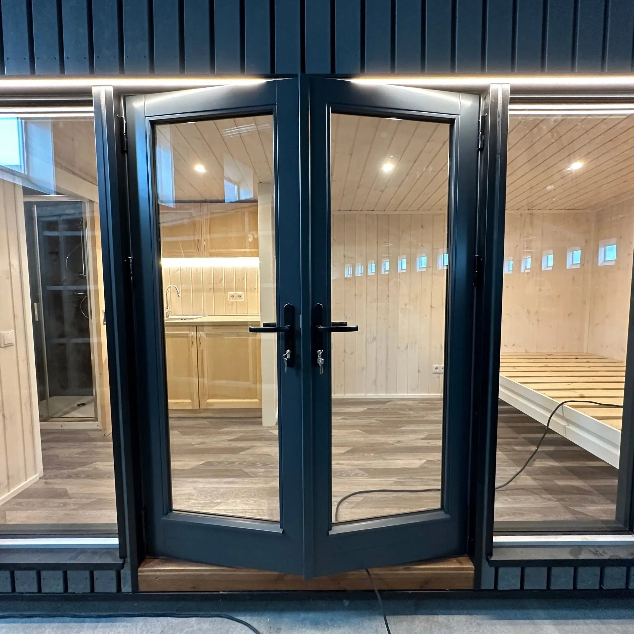 The Large GlampTainer container-style glamping unit – sleek black cladding exterior with full-glass double doors opening to timber interior