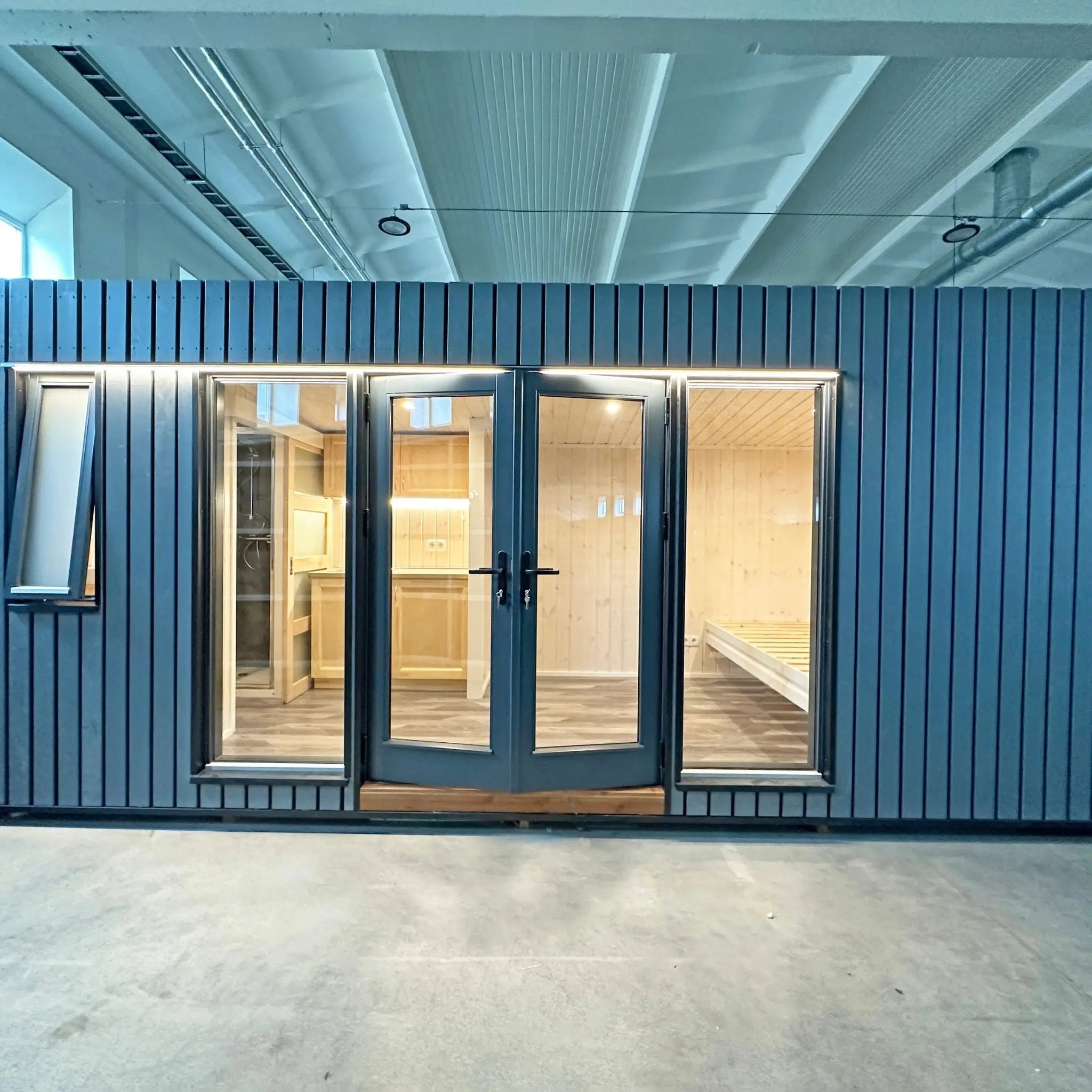 The Large GlampTainer container-style glamping unit – full frontal view with black vertical slat cladding, expansive glazing and bright interior