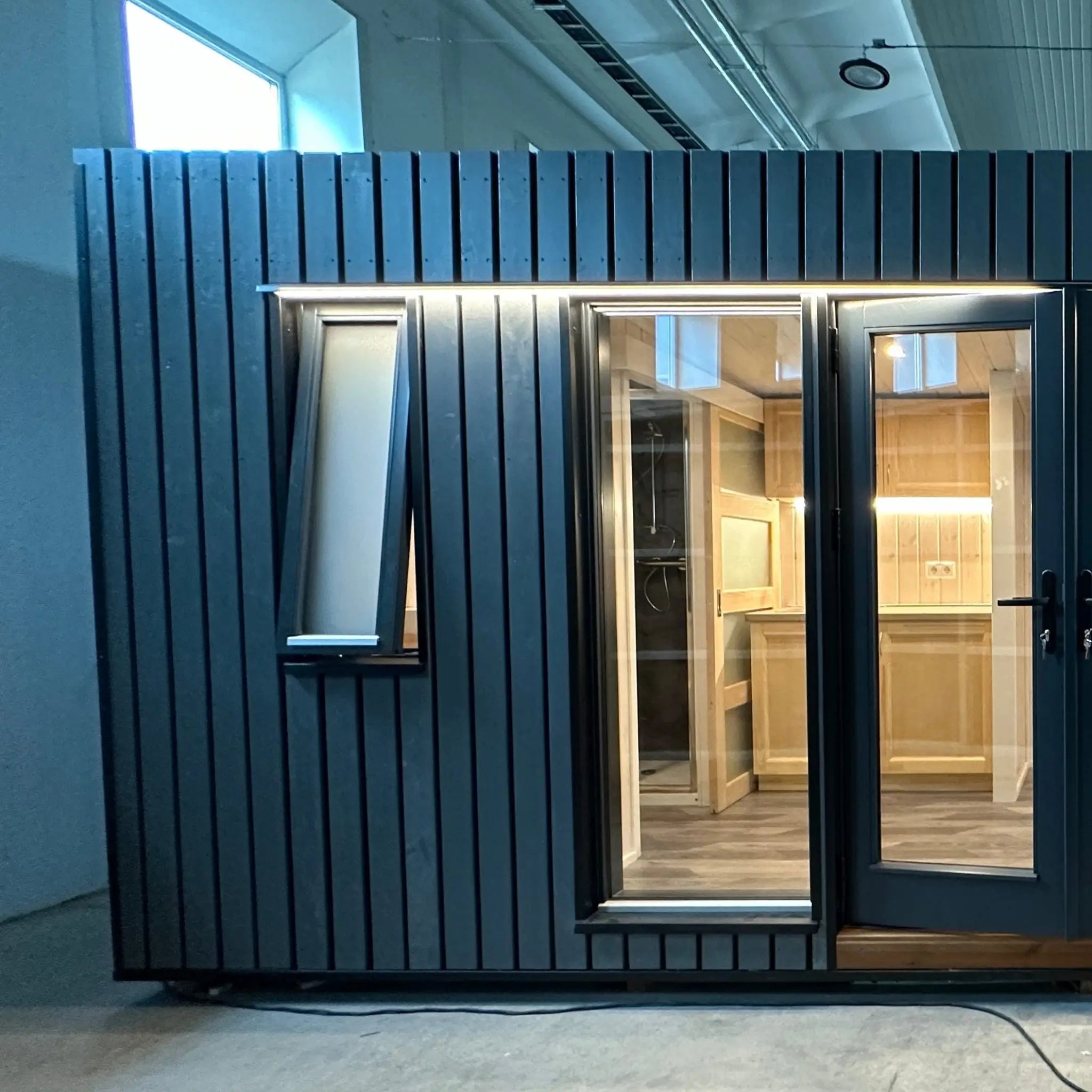 The Large GlampTainer container-style glamping unit – modern facade with dark timber cladding, large glazed doors and soft interior lighting