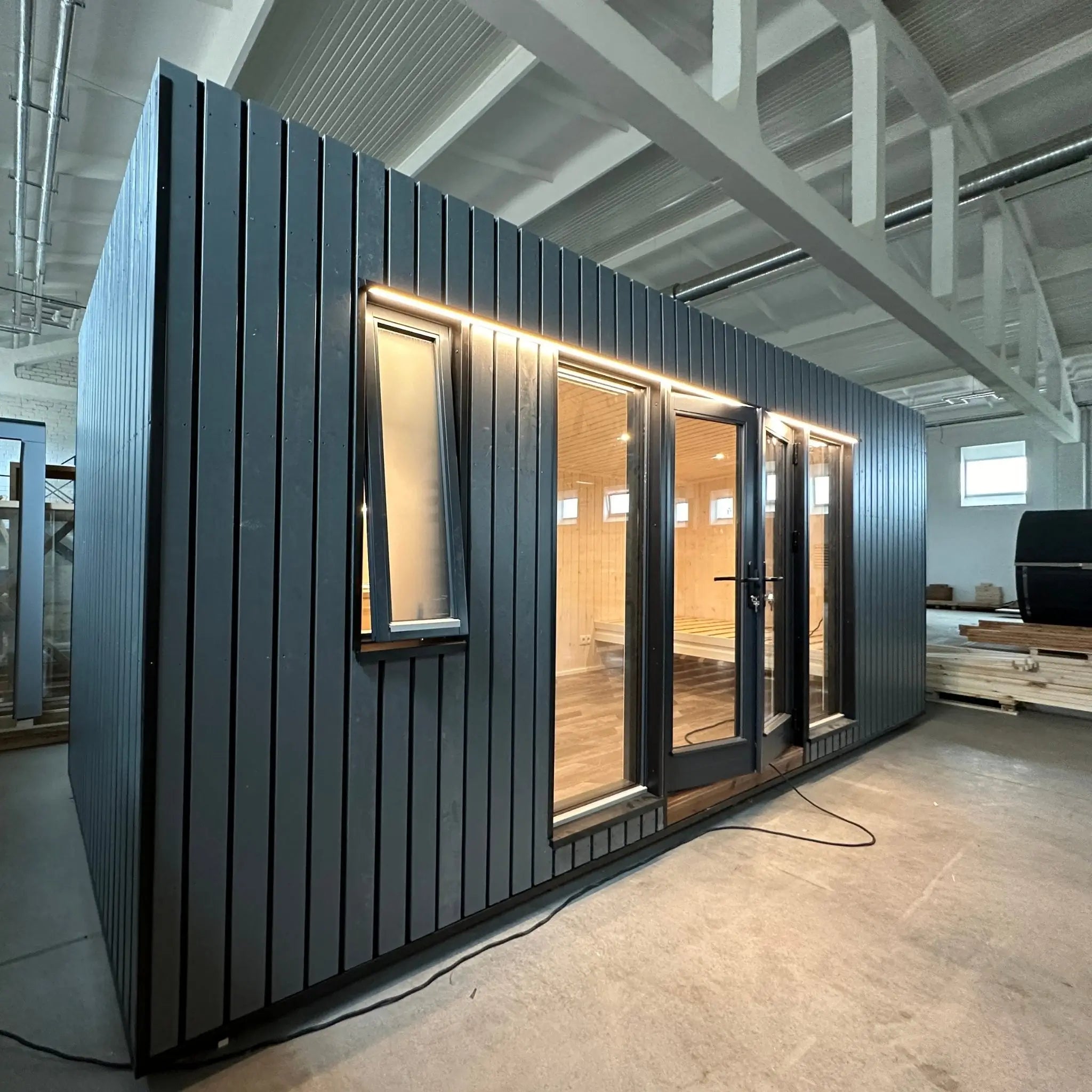 The Large GlampTainer container-style glamping unit – angled view of left side highlighting black slatted facade and slim side window