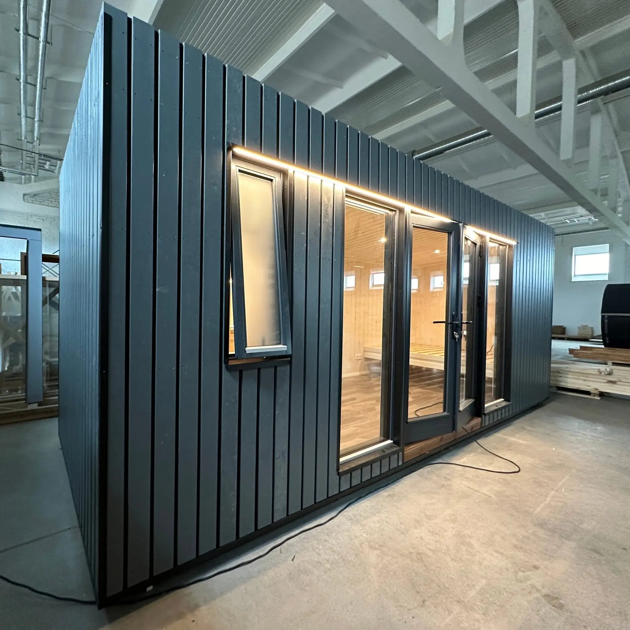 The Large GlampTainer container-style glamping unit – close-up of left side exterior showing slim window and matte black timber panelling