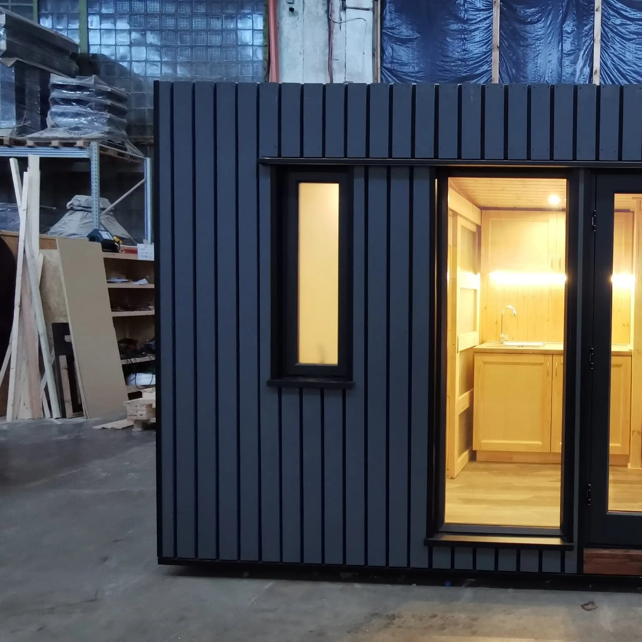The Medium GlampTainer container-style glamping structure – left side front view with closed doors, slim vertical window and warm-lit interior.